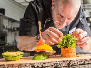 Koch des Schwarzwald Panoramas beim Zubereiten von kulinarischen Häppchen mit frischem Salat und gegrilltem Gemüse in Bio-Qualität