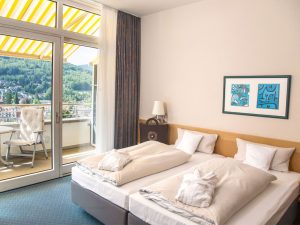 helles Hotelzimmer im Schwarzwald Panorama mit komfortablem Doppelbett und Balkon mit Ausblick auf den Ort und die Landschaft von Bad Herrenalb