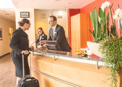 A businesswoman in front of the receptionist desk, being consulted by the staff of the hotel SCHWARZWALD PANORAMA