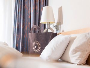 A decorative brown bag with the SCHWARZWALD PANORAMA logo on it is located next to a bed with white linen.