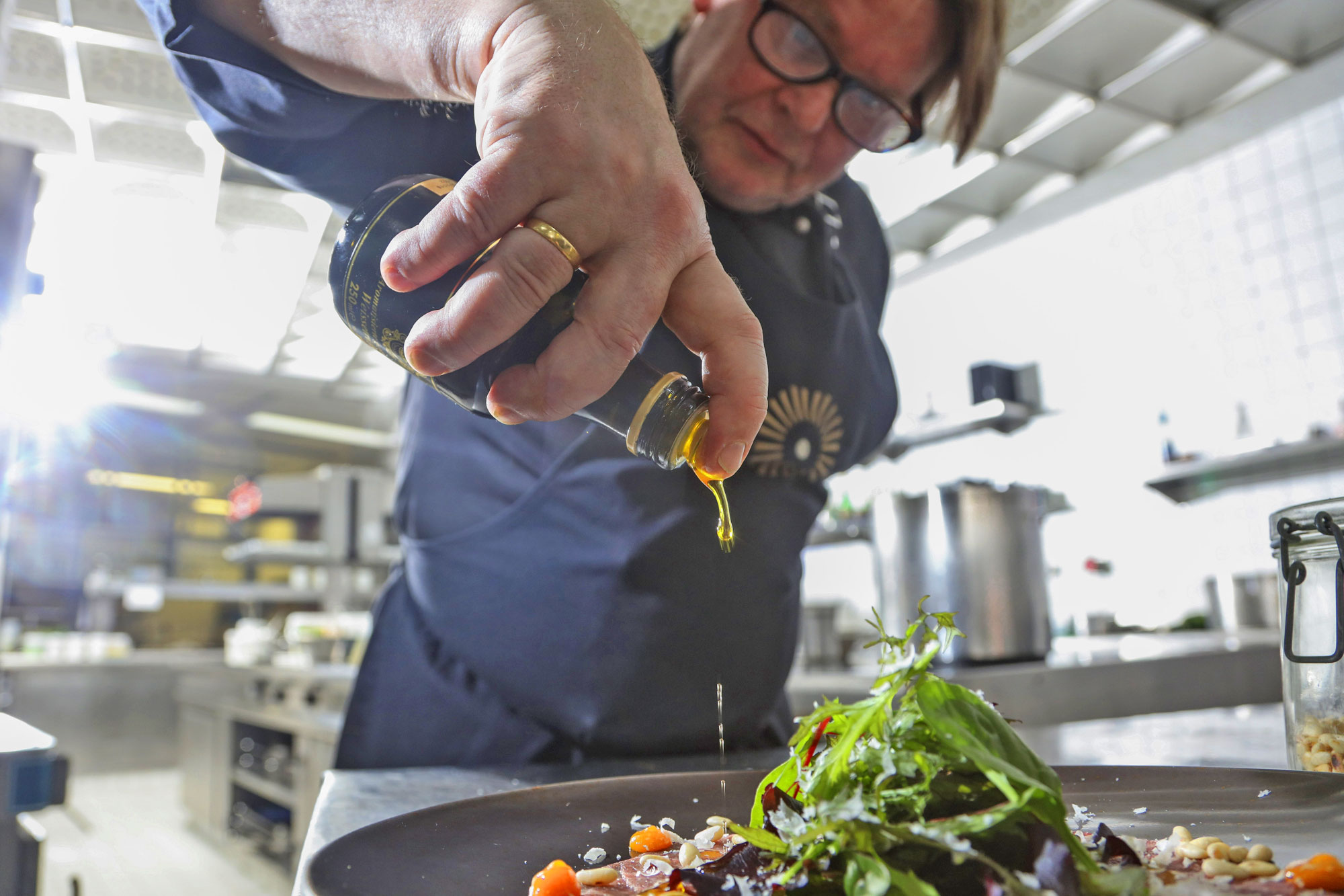 Koch im Schwarzwald Panorama beträufelt ein fertig angerichteten Salat mit hochwertigem Öl