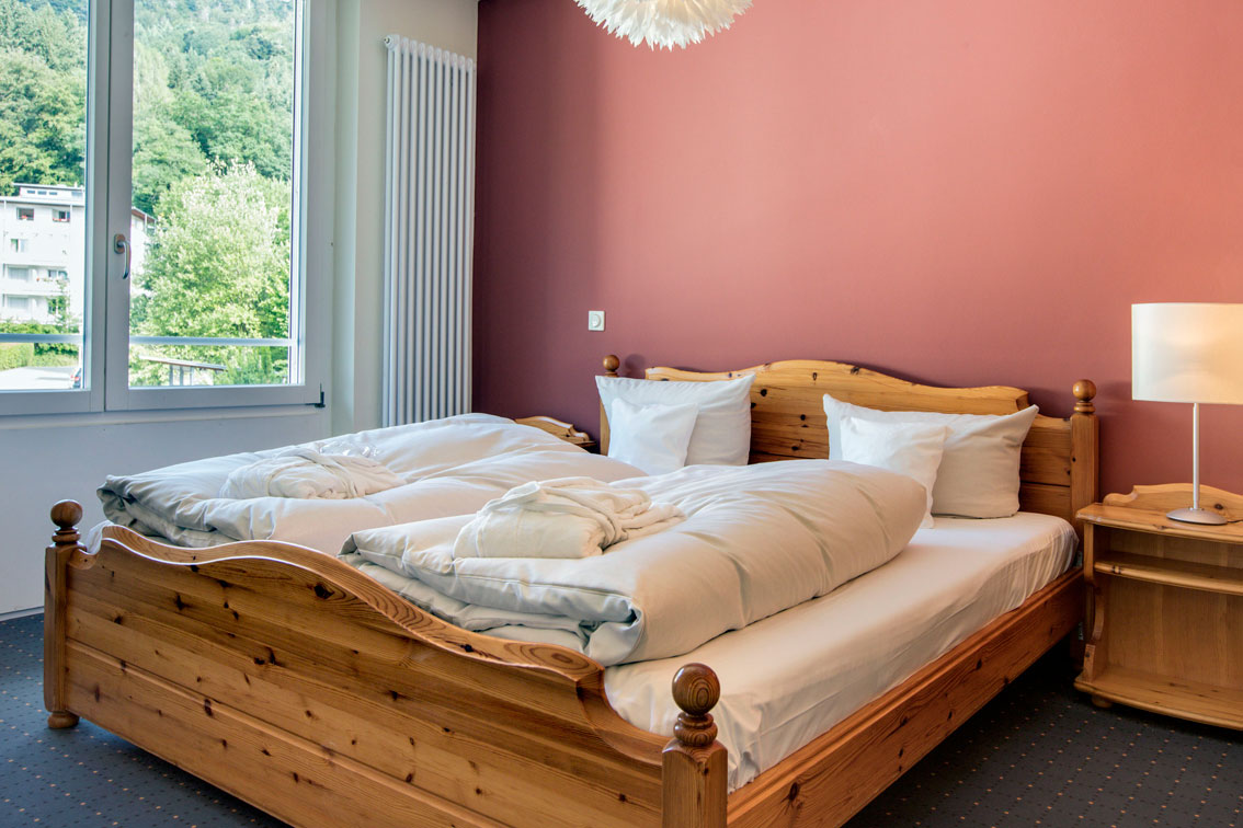 A wooden bed in a room with brown wall paint in the Hotel Schwarzwald Panorama. In the background a a panoramic view is seen
