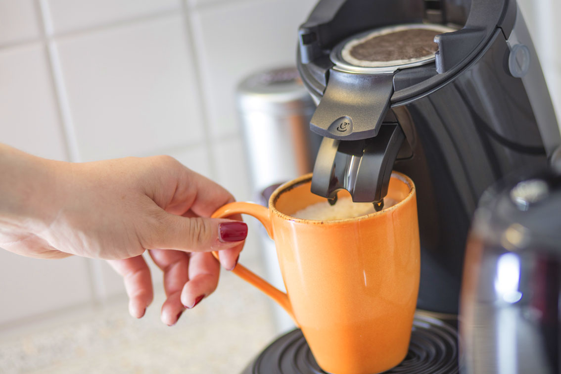 Someone using a coffee machine to fill coffee in to an orange mug in the Hotel Schwarzwald Panorama