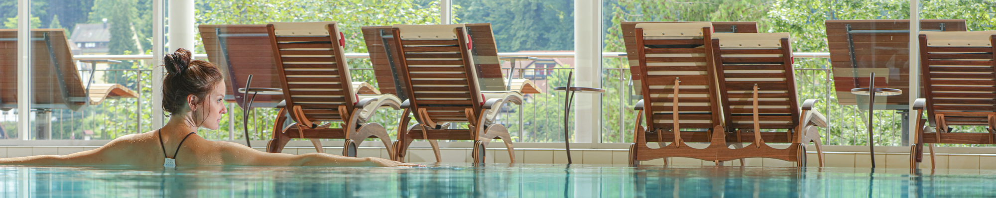 Eine Frau nimmt ein Bad im SPA, Wellness, Pool Bereich, vor Liegestühlen und grüner Kulisse im Hotel Schwarzwald Panorama.