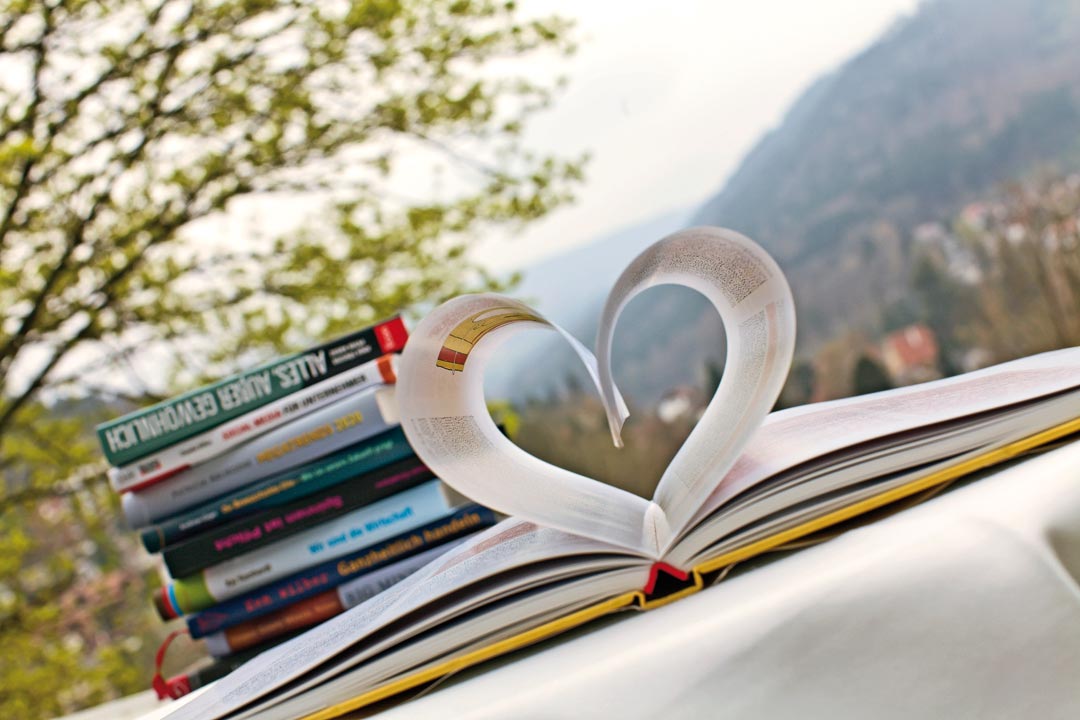 Ein Herz geformt aus Buchseiten steht neben einem Stapel Bücher, im Hintergrund ist die Aussicht vom Hotel SCHWARZWALD PANORAMA zu sehen.